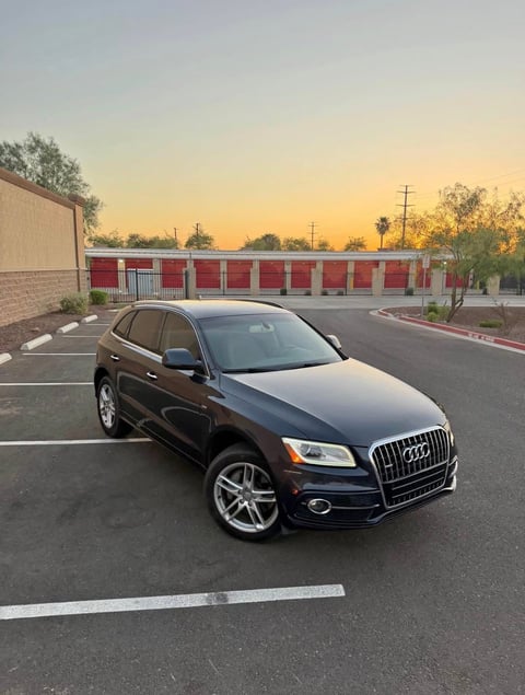 Black Audi Q5 SUV parked in empty lot at sunset with red brick buildings in background