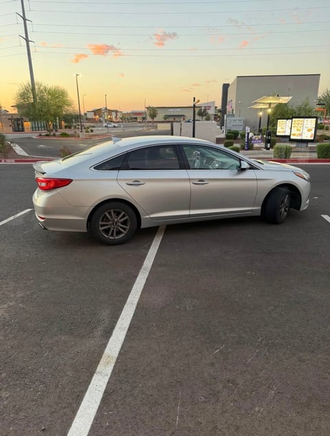 Silver sedan parked in an empty lot at sunset with commercial buildings