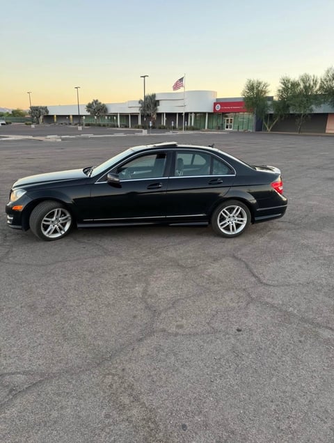 Black sedan parked in empty parking lot with commercial buildings at dusk