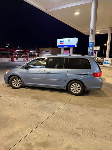 Blue minivan parked at a gas station at night with pump number 9 visible