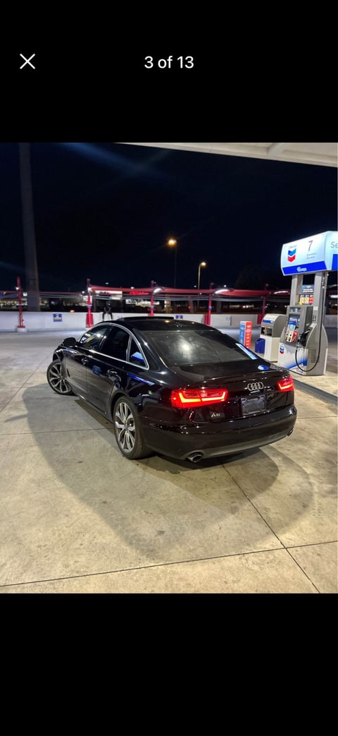 Black Audi A6 sedan parked at a gas station during nighttime with illuminated tail lights