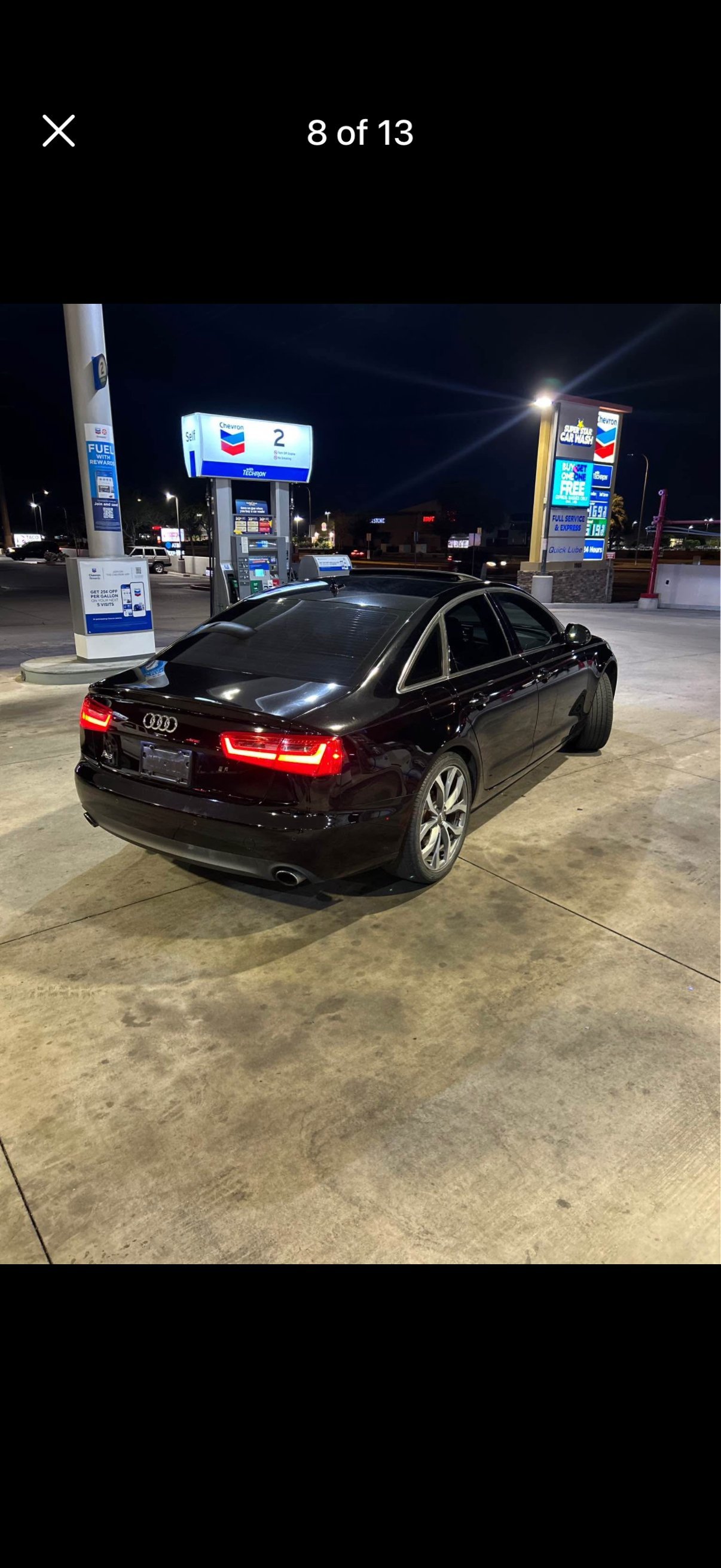 Black Audi sedan parked at night at a gas station with illuminated signage