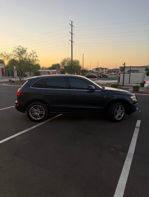 Black SUV parked in empty lot at sunset with power lines and commercial buildings