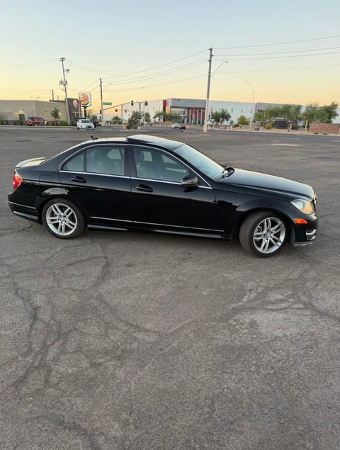 Black sedan parked in an empty lot at sunset with buildings