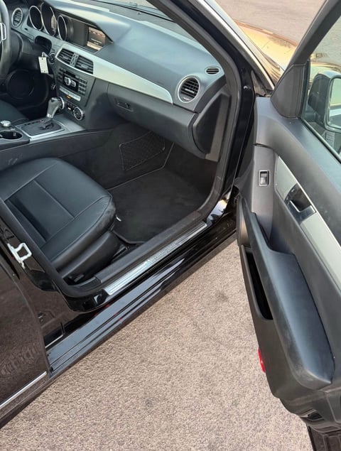 Interior view of black car with open driver-side door showing steering wheel and black leather seat