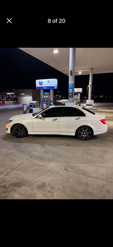 White sedan parked at a Chevron gas station at night with illuminated pumps in the background