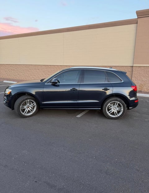 Black Audi SUV parked in empty parking lot beside beige building at dusk