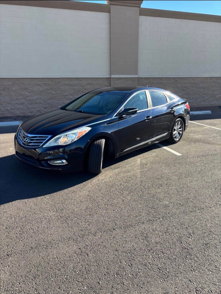 Black Hyundai Azera sedan parked in empty parking lot in front of concrete building wall