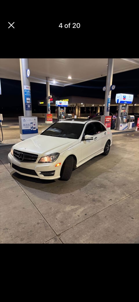 White Mercedes-Benz C-Class sedan parked at a gas station at night with illuminated canopy and fuel pumps in background