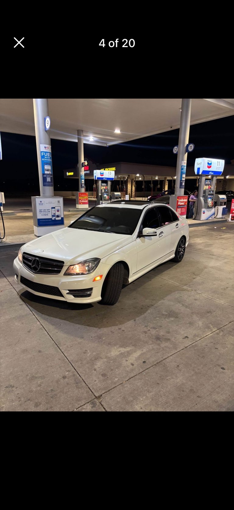 White Mercedes-Benz C-Class sedan parked at a gas station at night with illuminated canopy and fuel pumps in background